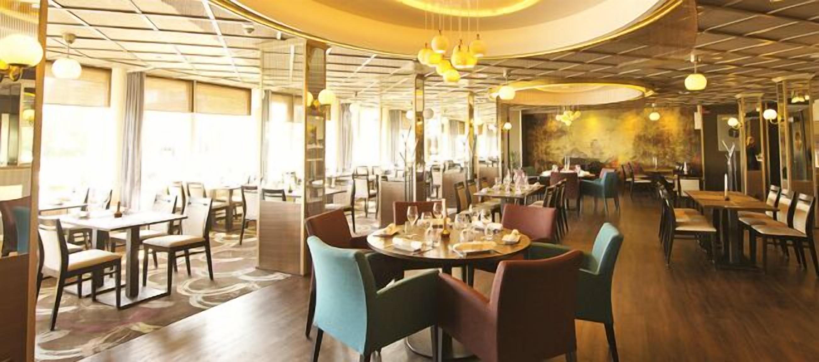 Een restaurant met ronde tafels, stoelen en hangende lampen.