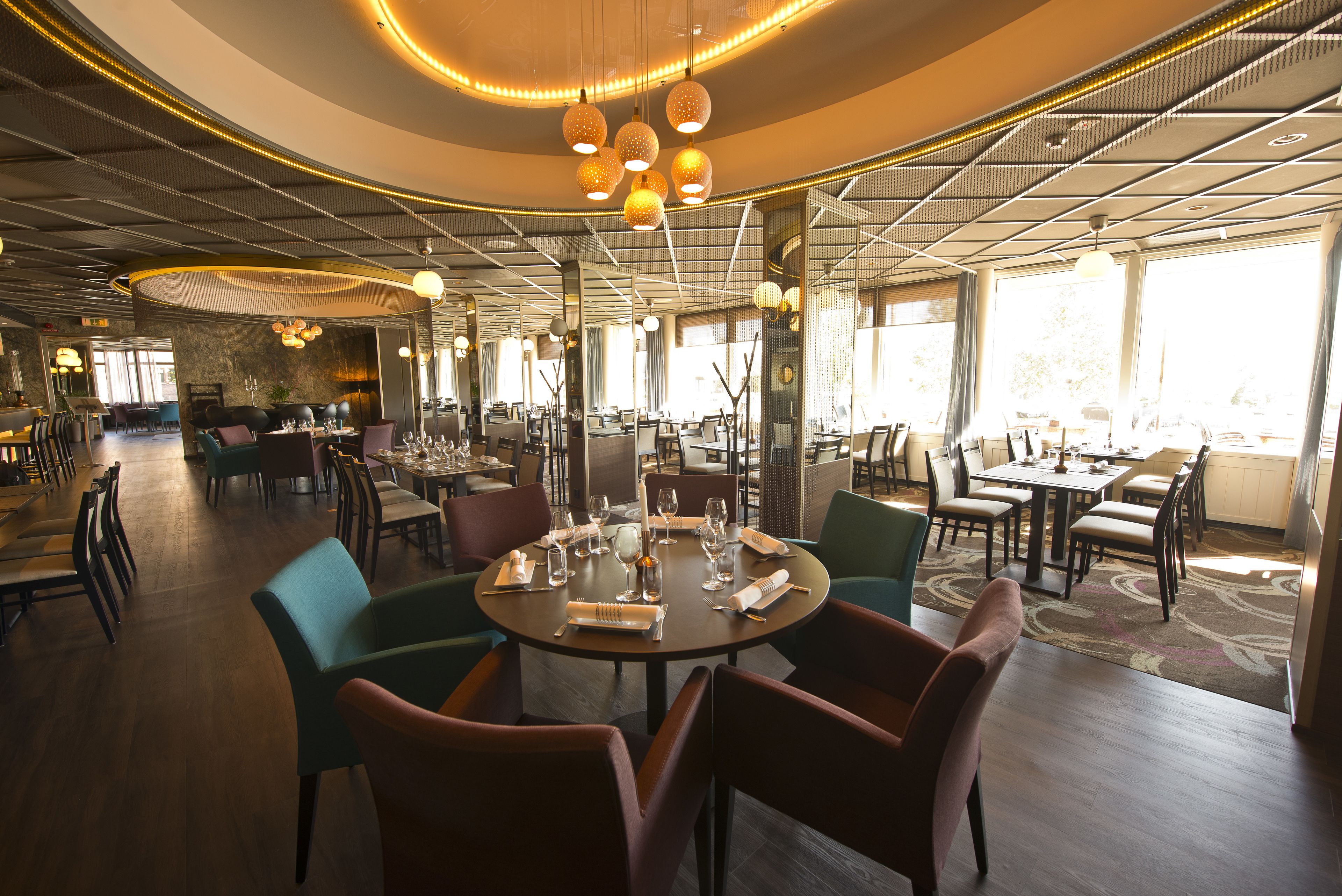 Un restaurant moderne avec des tables rondes, des chaises et des luminaires suspendus.