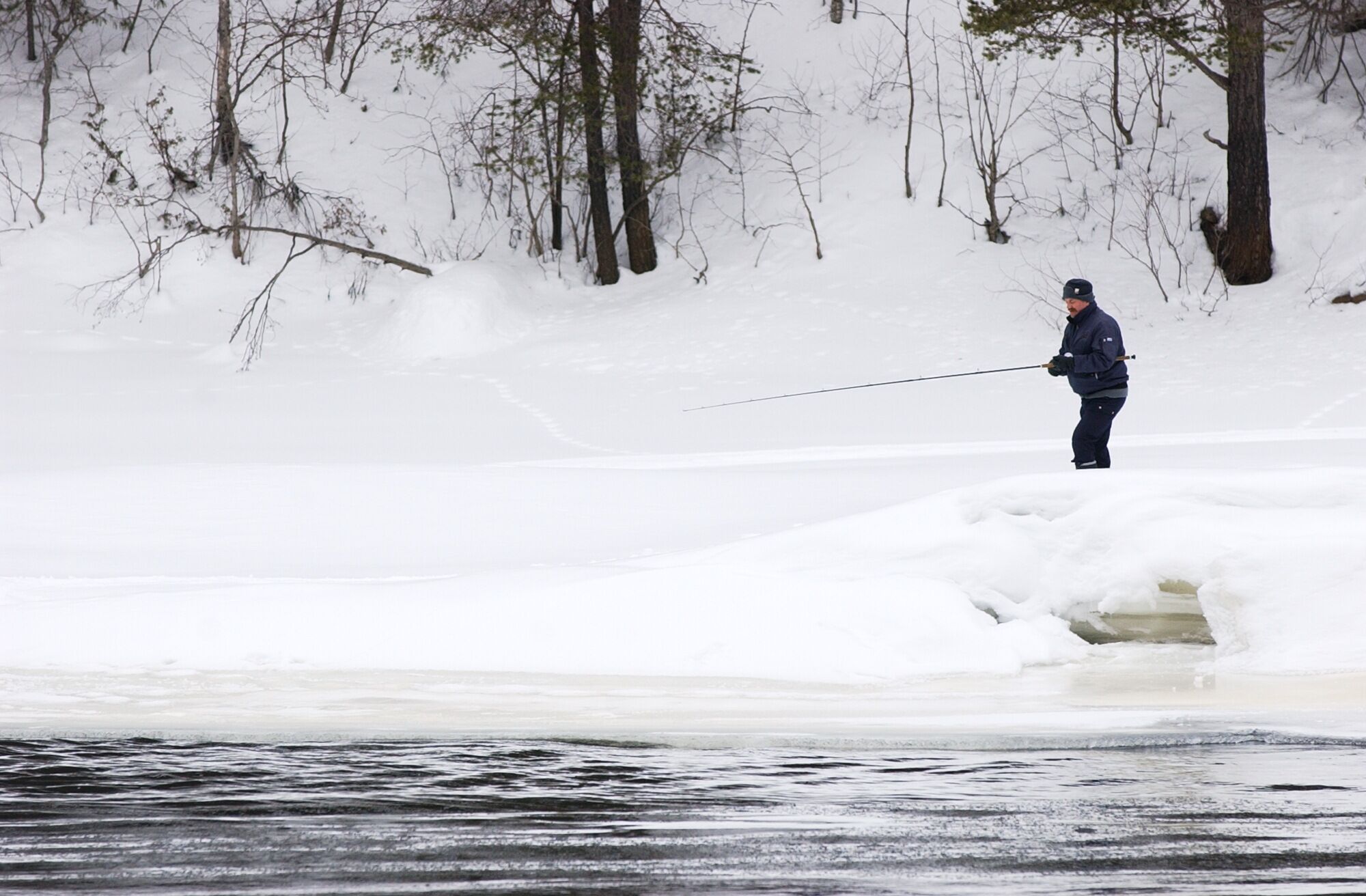 A person fishing on a frozen lake surrounded by trees.