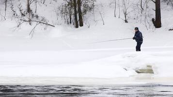 A person fishing on a frozen lake surrounded by trees.