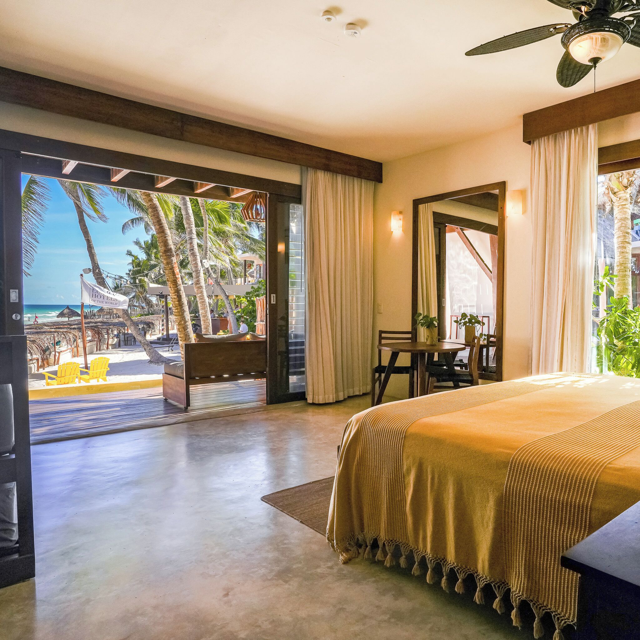 A hotel room with a bed, a desk, and a view of the beach and palm trees.