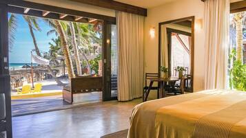 A hotel room with a bed, a desk, and a view of the beach and palm trees.