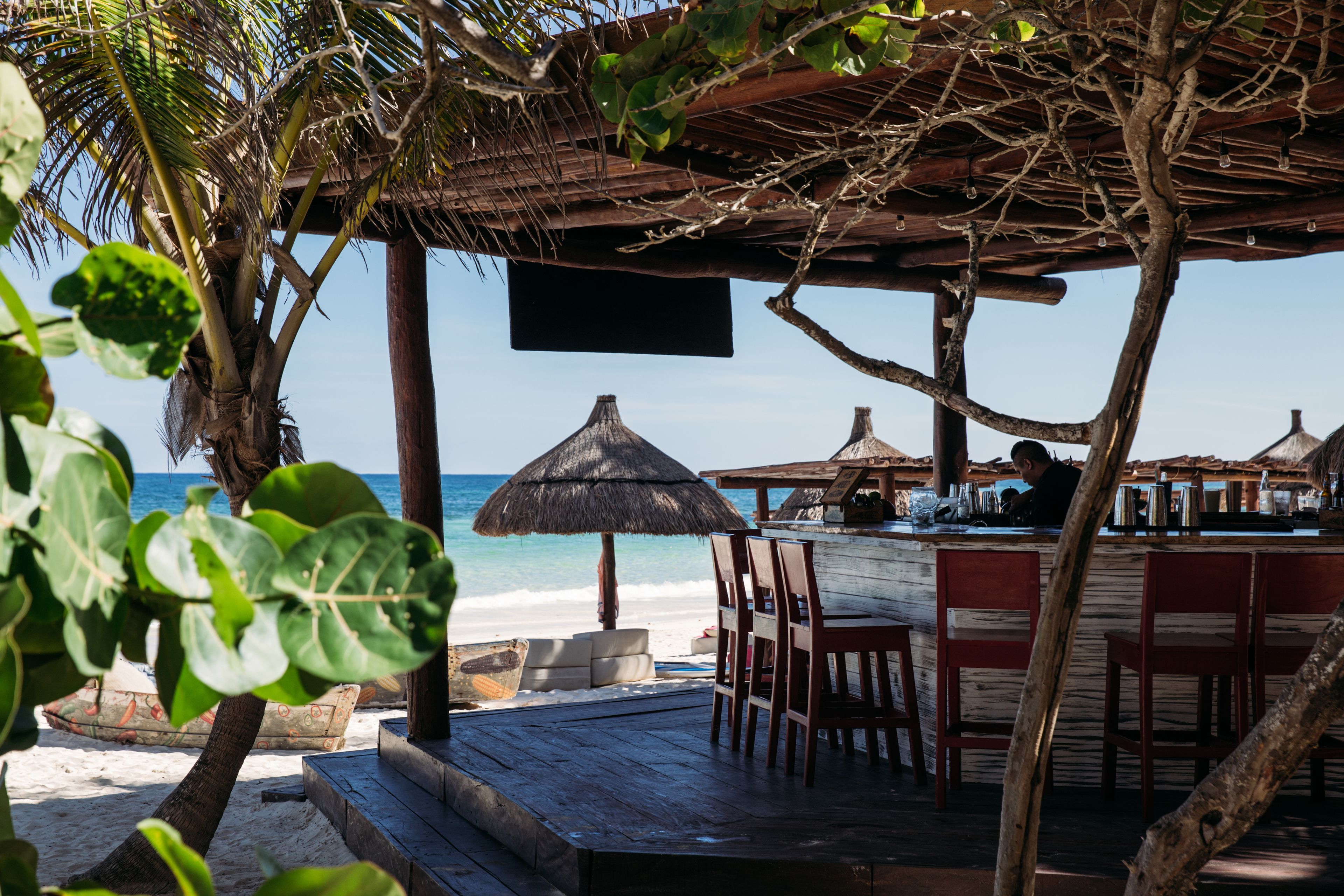 A beachside bar with wooden furniture and thatched umbrellas, overlooking the ocean.