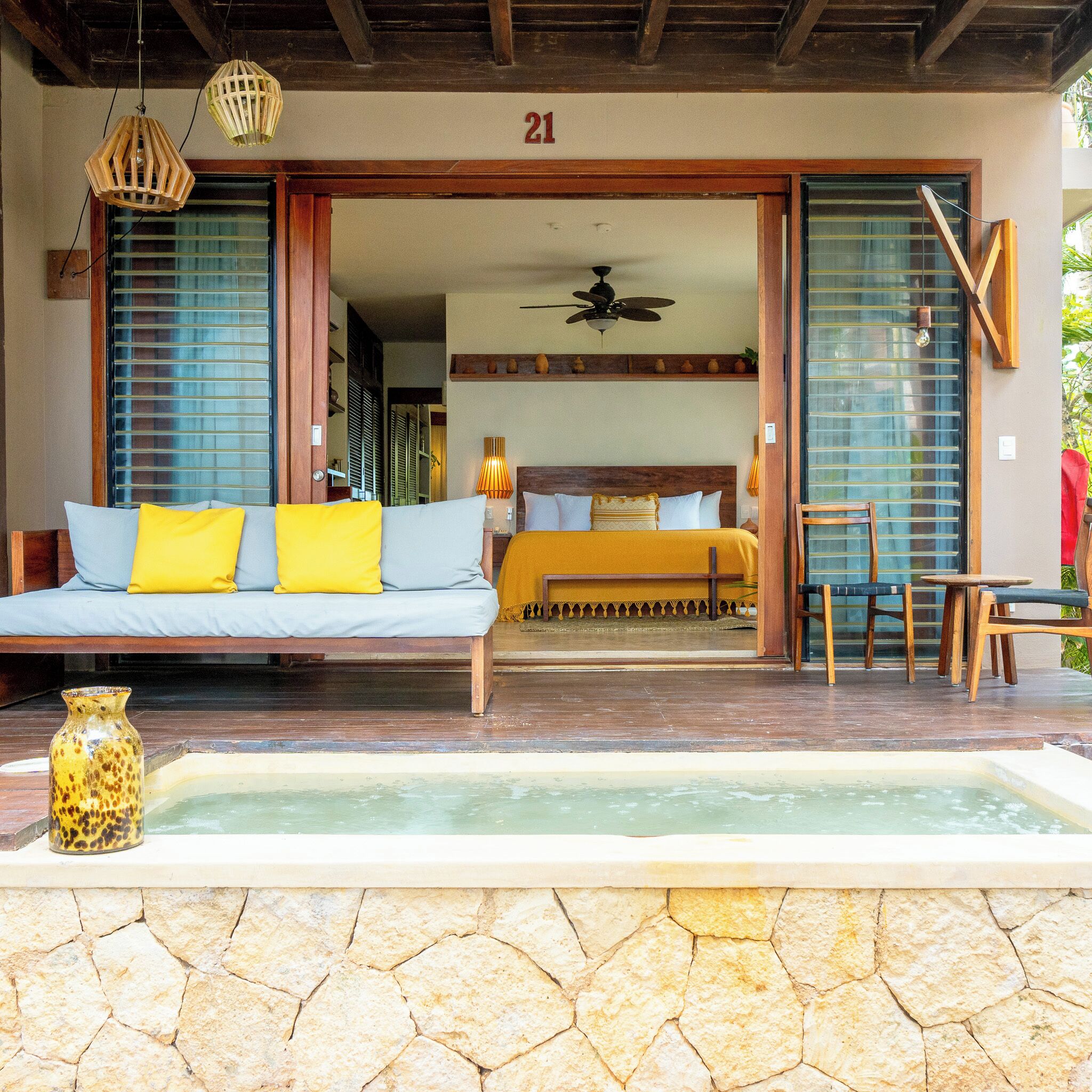 A room with a bed, a sofa, a table, chairs, a ceiling fan, and a water feature.