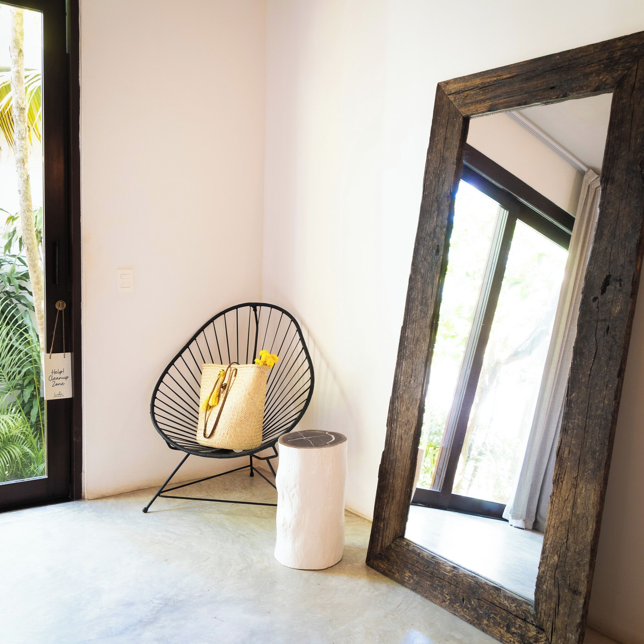 Una habitación con un espejo grande, una silla de mimbre y un taburete pequeño.