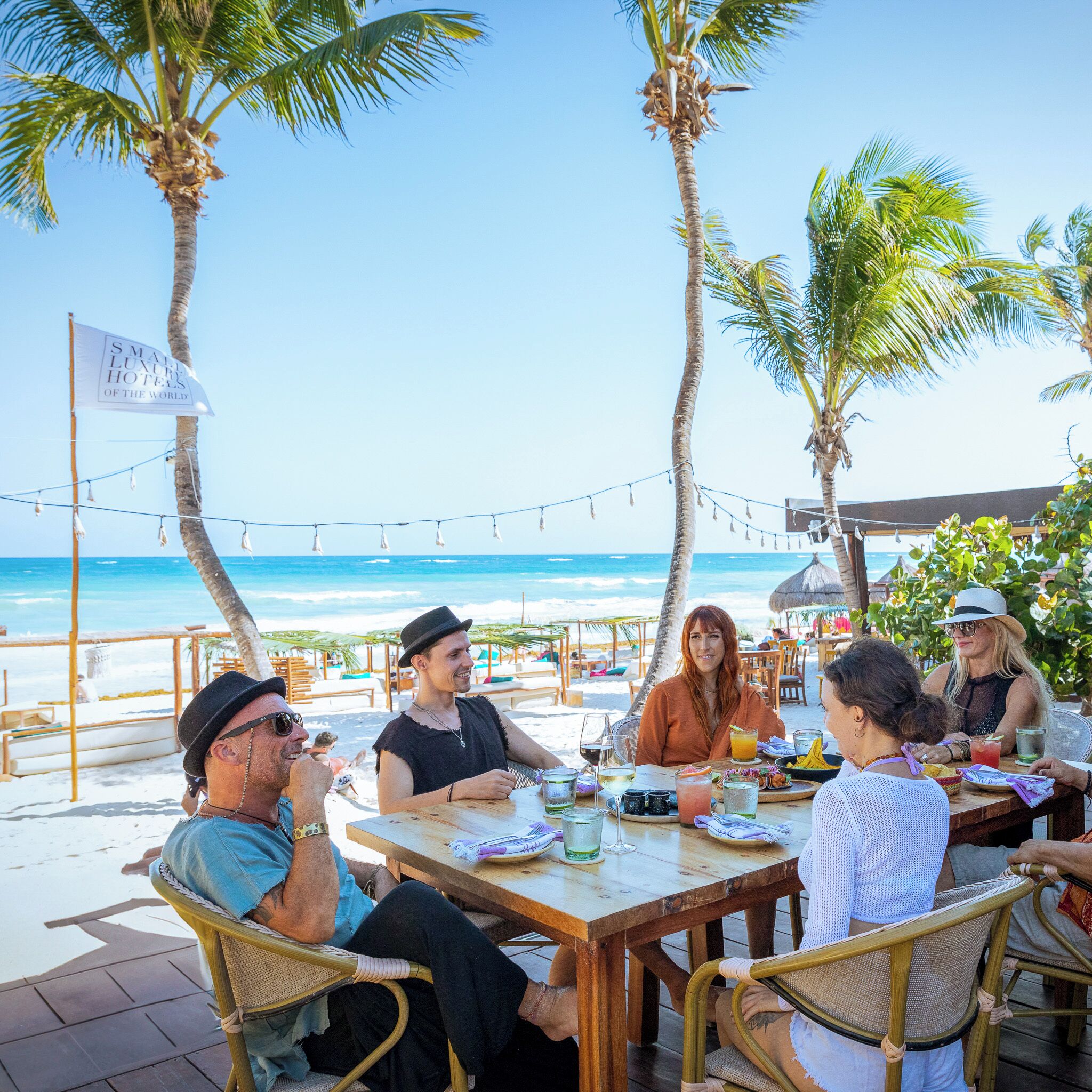 A group of people dining at an outdoor table with a view of the beach and ocean.