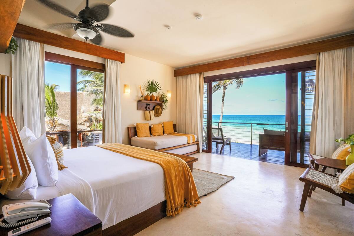 Une chambre d’hôtel avec un grand lit, un canapé, un balcon avec vue sur l’océan et un ventilateur de plafond.