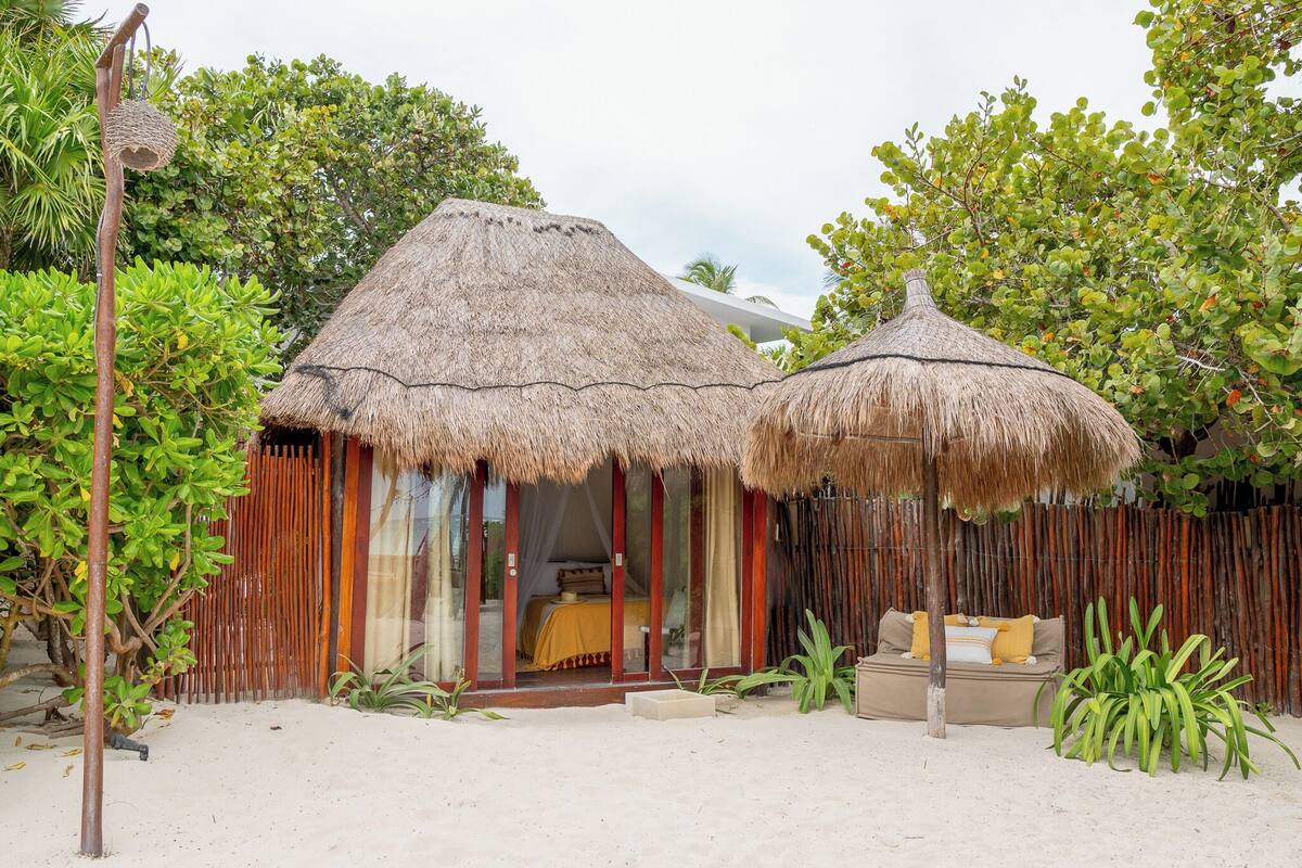 Un bungalow au toit de chaume comprenant un lit, un petit coin salon et une vue sur la végétation environnante.