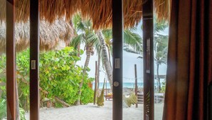 A beach view through a wooden-framed window with curtains, palm trees, and a sandy beach. - La Zebra Tulum - a Small Luxury Hotel (Tulum)