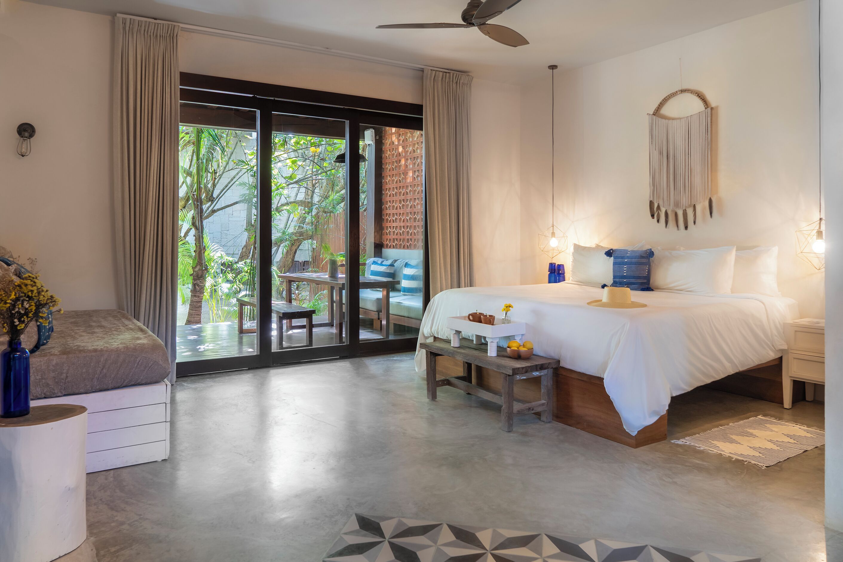 Quarto com cama, mesa de cabeceira, cadeira e vista para o exterior.