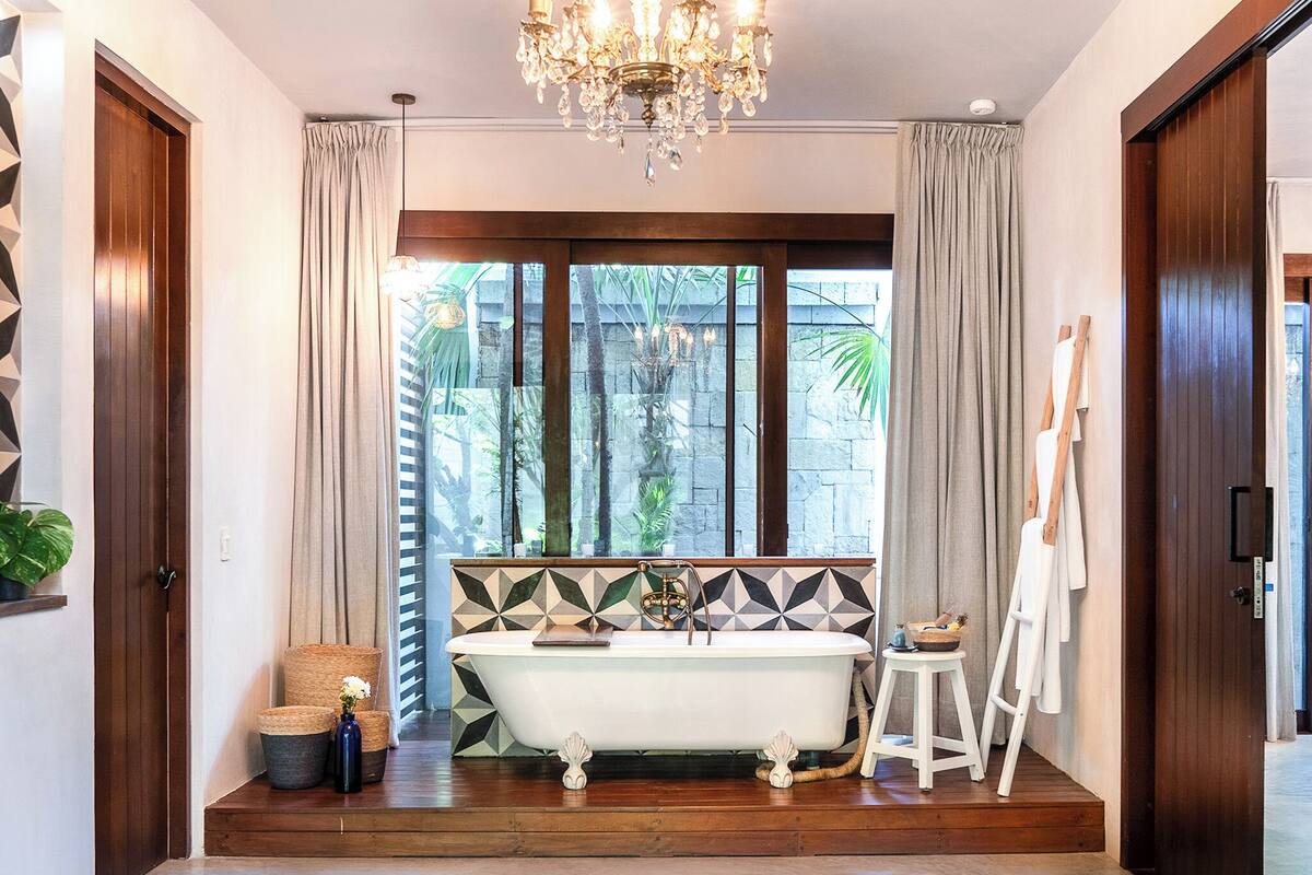 Une salle de bain avec une baignoire sur pieds, un lustre et une vue sur l’extérieur.