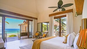 A bedroom with a large bed, a desk, and a chair, a balcony with a view of the ocean, and a ceiling fan. - La Zebra Tulum - a Small Luxury Hotel (Tulum)