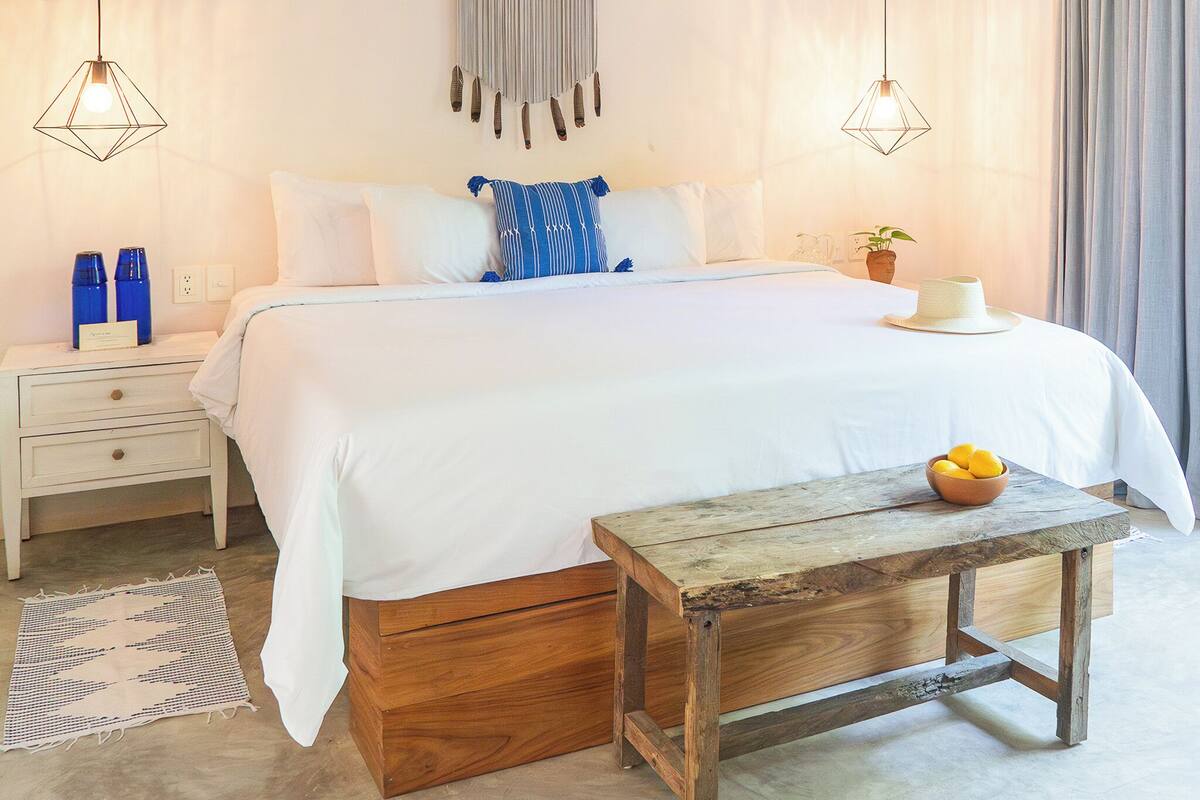 A bedroom with a bed, bedside tables, a wooden bench, and a wall hanging.