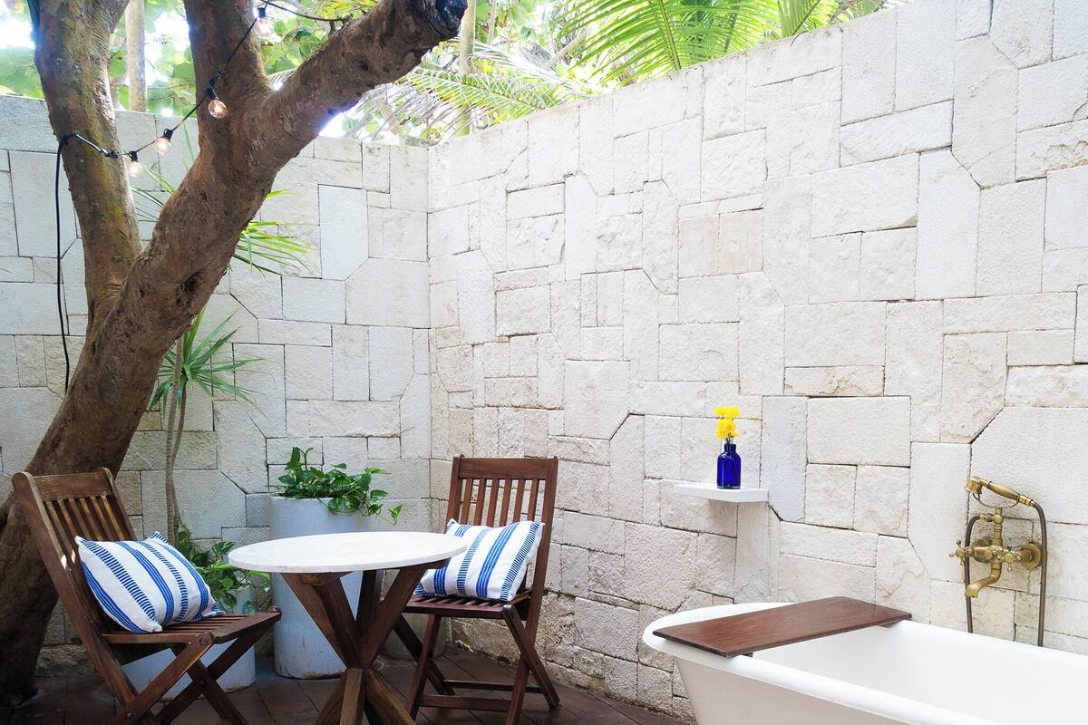 Une terrasse en bois avec une baignoire blanche, deux chaises en bois dotées de coussins à rayures et une petite table.