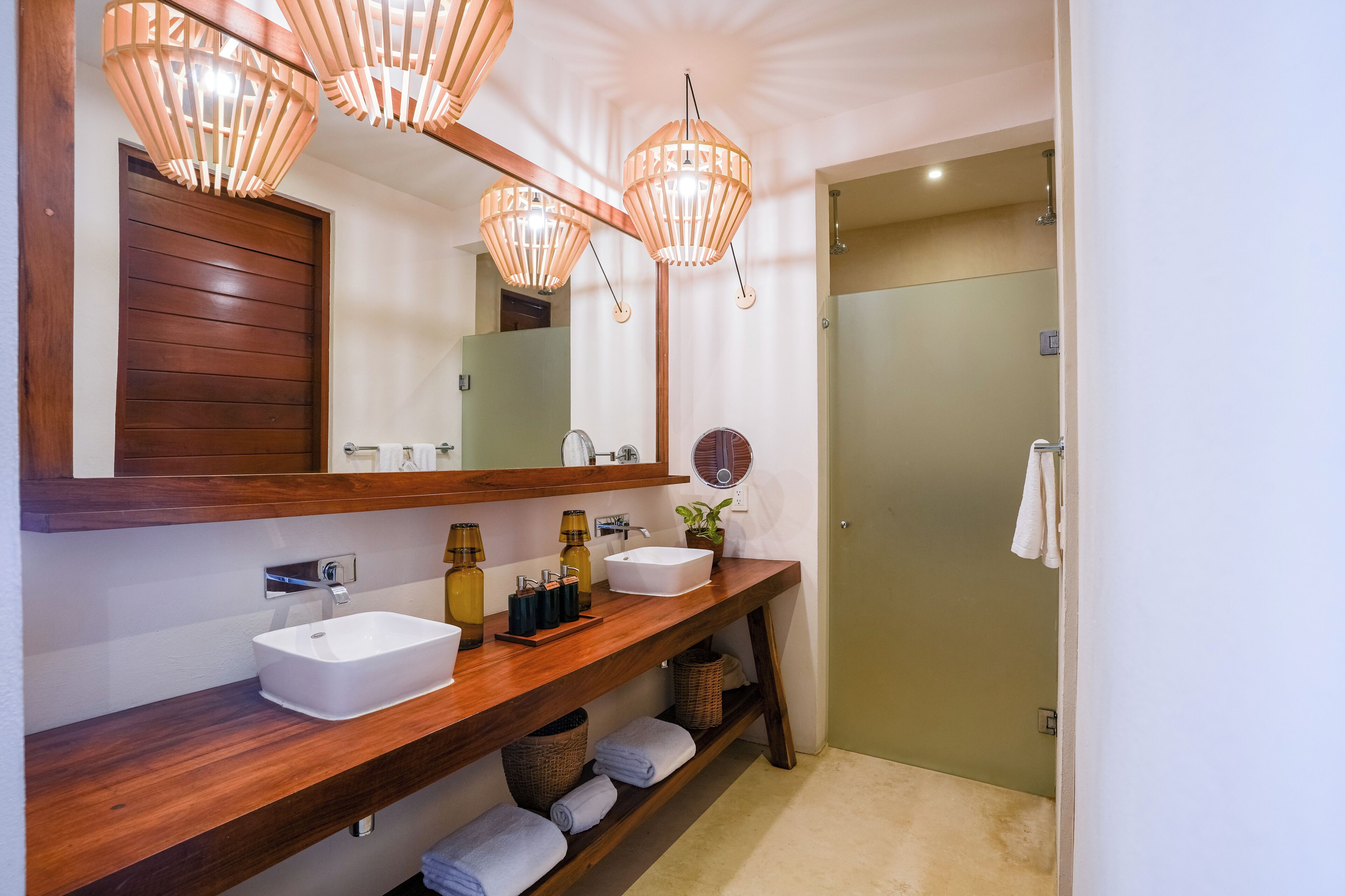 A bathroom with a wooden vanity, two sinks, a mirror, and a shower.
