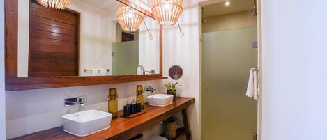 A bathroom with a wooden vanity, two sinks, a mirror, and a shower.