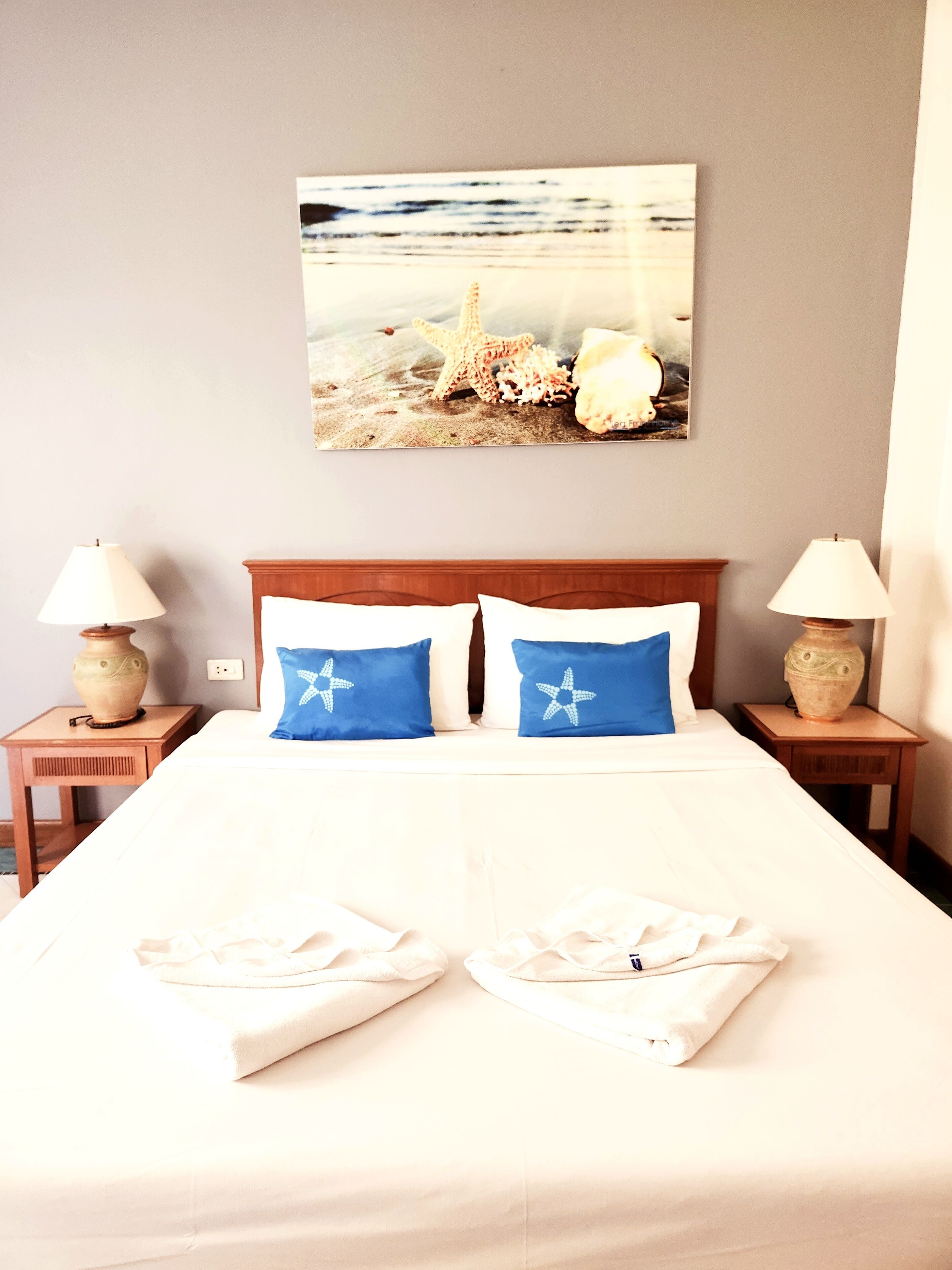 A neatly made bed with two blue pillows, a wooden headboard, and a wall-mounted picture of a beach scene.