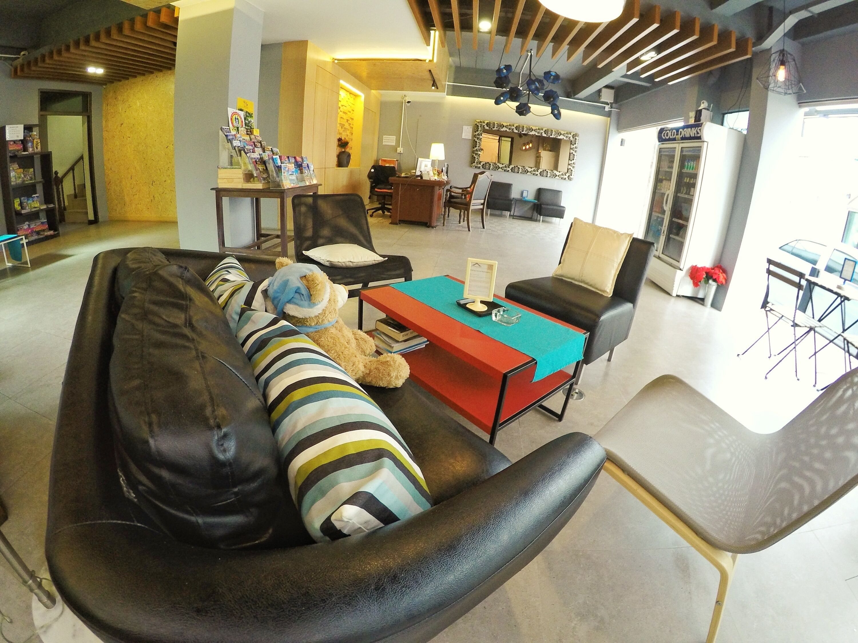 A modern living room with a sofa, a coffee table, and a teddy bear. There is a reception desk with a mirror and a refrigerator in the background.