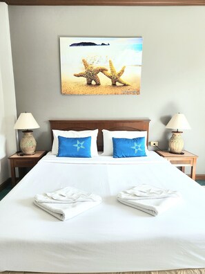 A hotel room with a bed, two nightstands, lamps, a painting of sea creatures, and two towels on the bed. - Sea Front Home Boutique - Patong Beach (Patong)