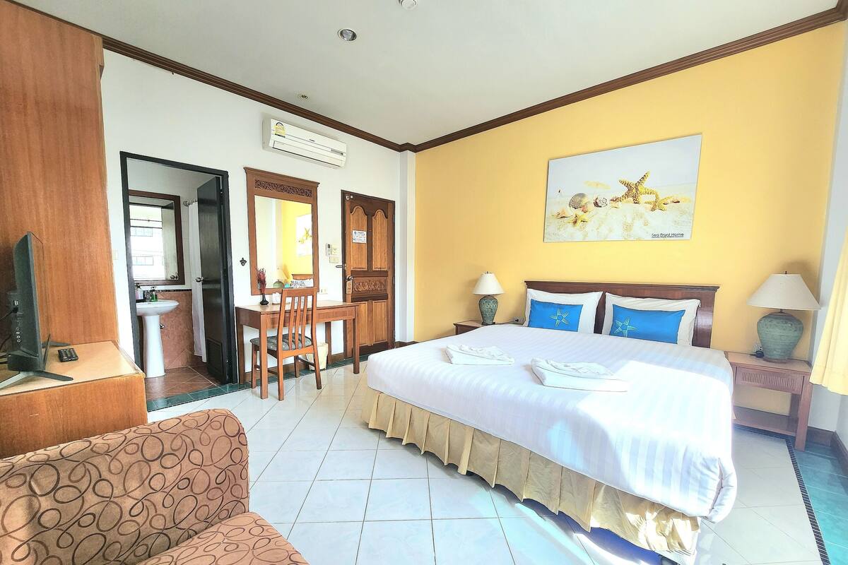 A hotel room with a bed, a desk, a chair, a sofa, and a television.