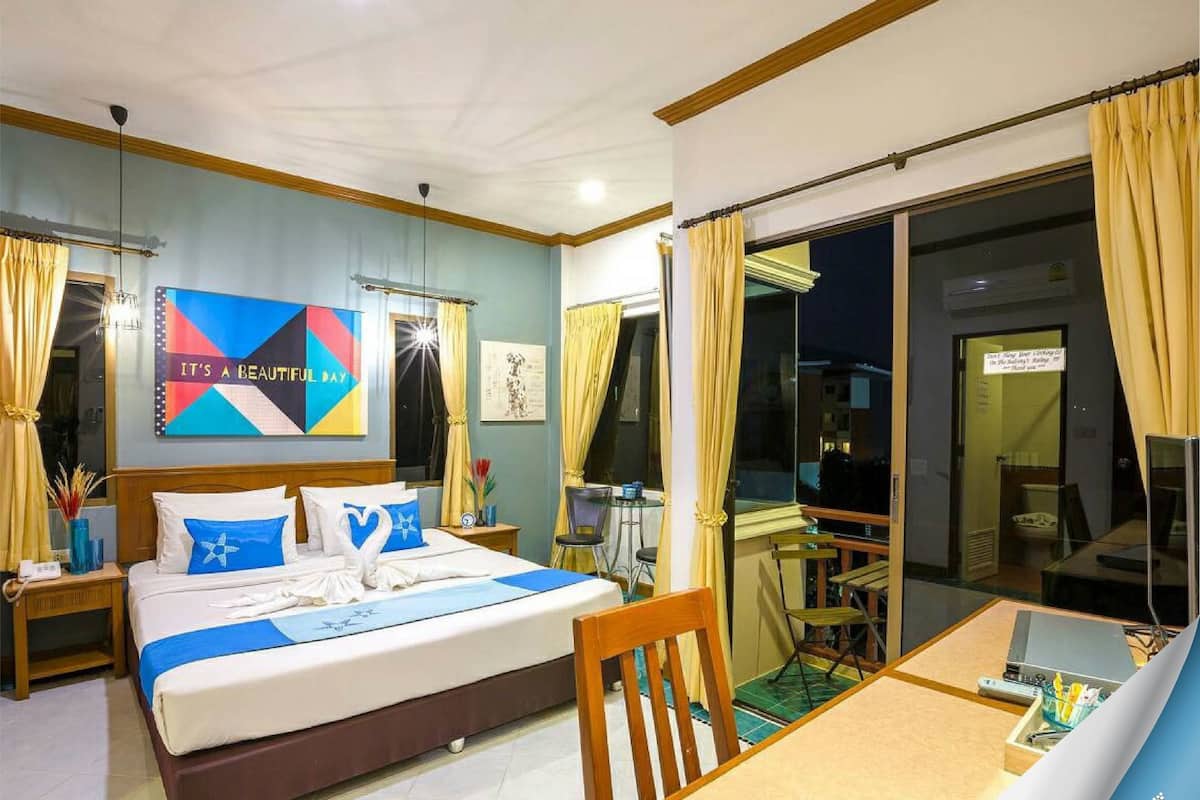 A hotel room with a bed, a desk, a chair, a large window, and a sliding door to a balcony.