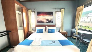 Habitación de hotel con una cama grande, un cuadro en la pared y un balcón con mesa y sillas.