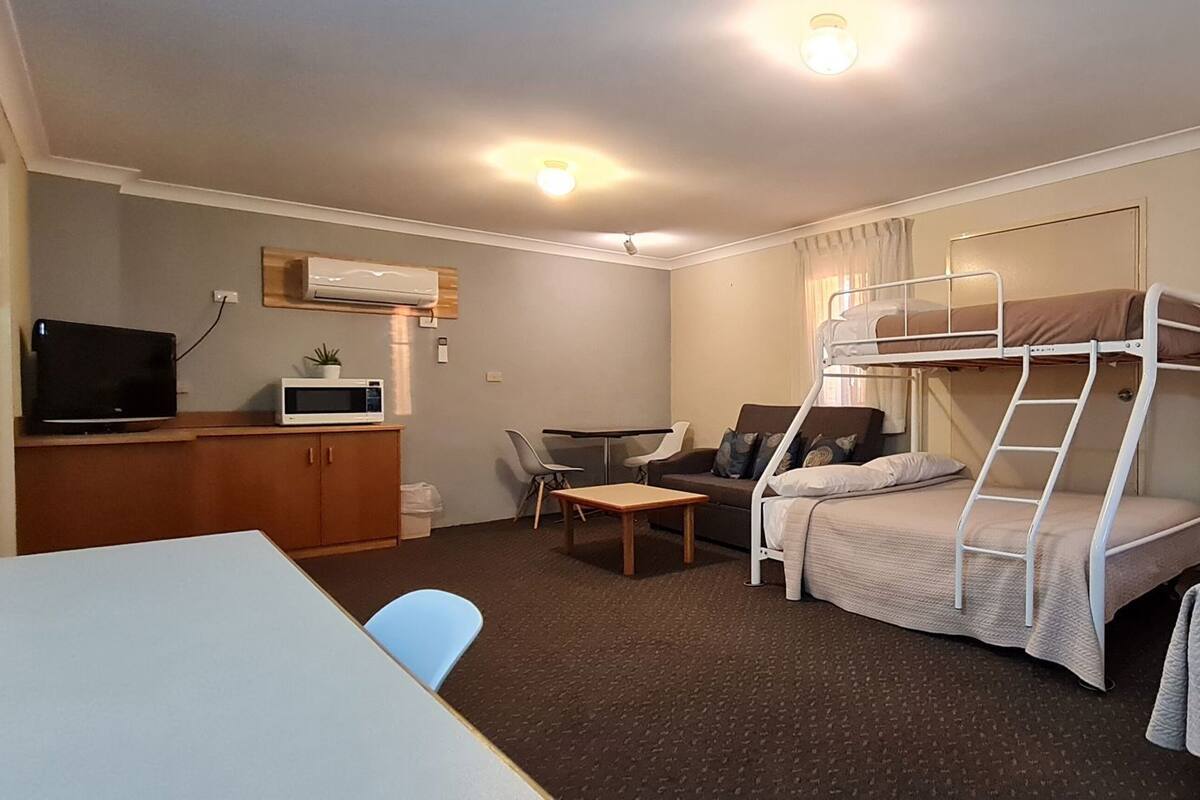 A hotel room with bunk beds, a desk with a TV, a microwave, a chair, and a small table.