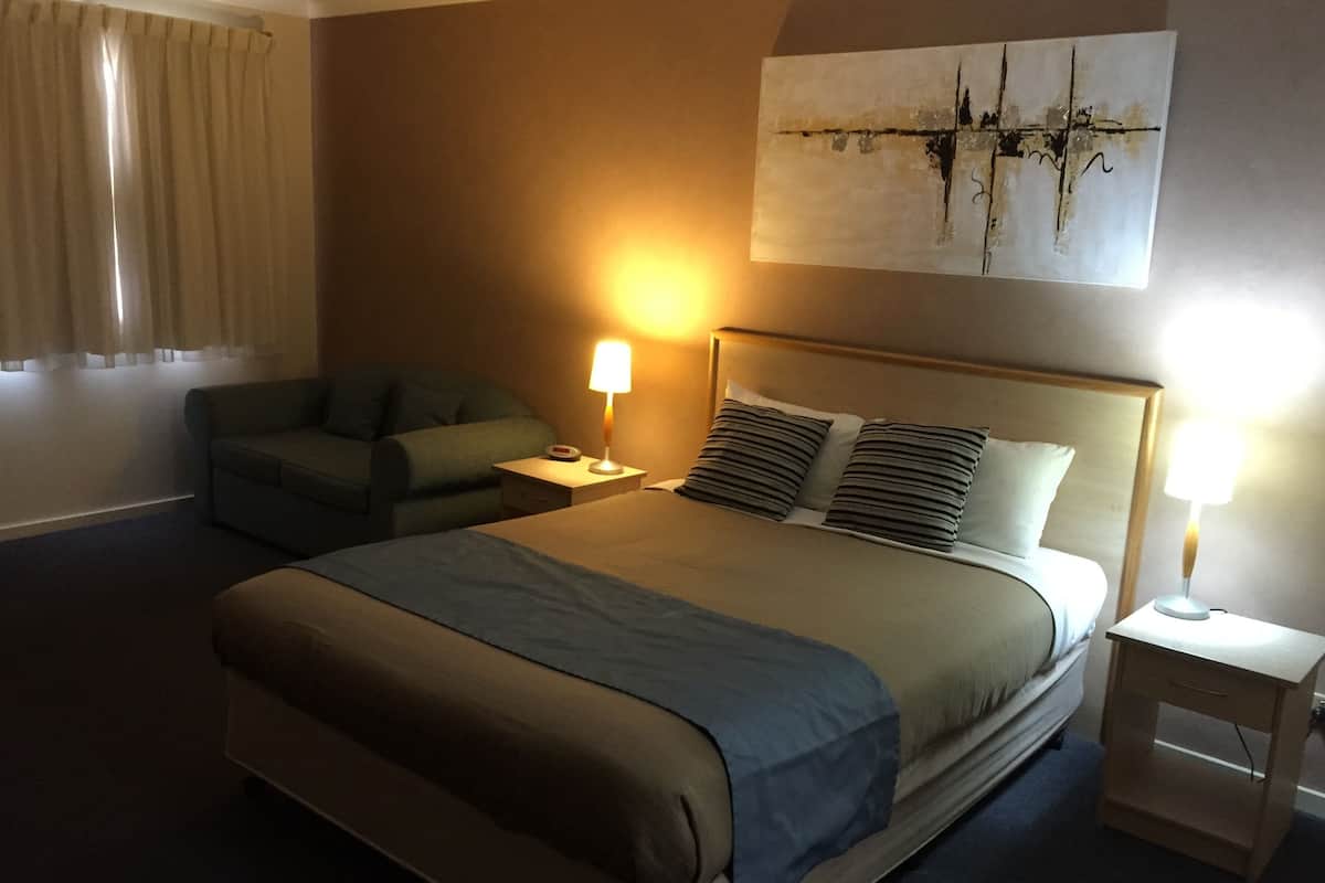 A hotel room with a bed, two bedside tables, a nightstand, a couch, and a painting on the wall.