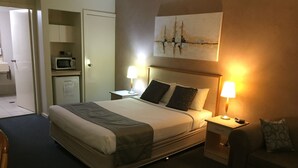 Habitación de hotel con cama, mesitas de noche, lámpara, microondas, sofá y un cuadro en la pared.