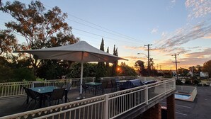 Un patio al aire libre con mesas y sillas, una zona cubierta y una piscina.