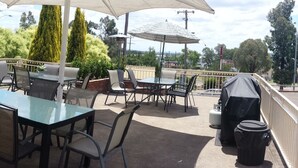 Un patio al aire libre con mesas y sillas, una zona de estar cubierta y vistas de la vegetación y edificios circundantes.