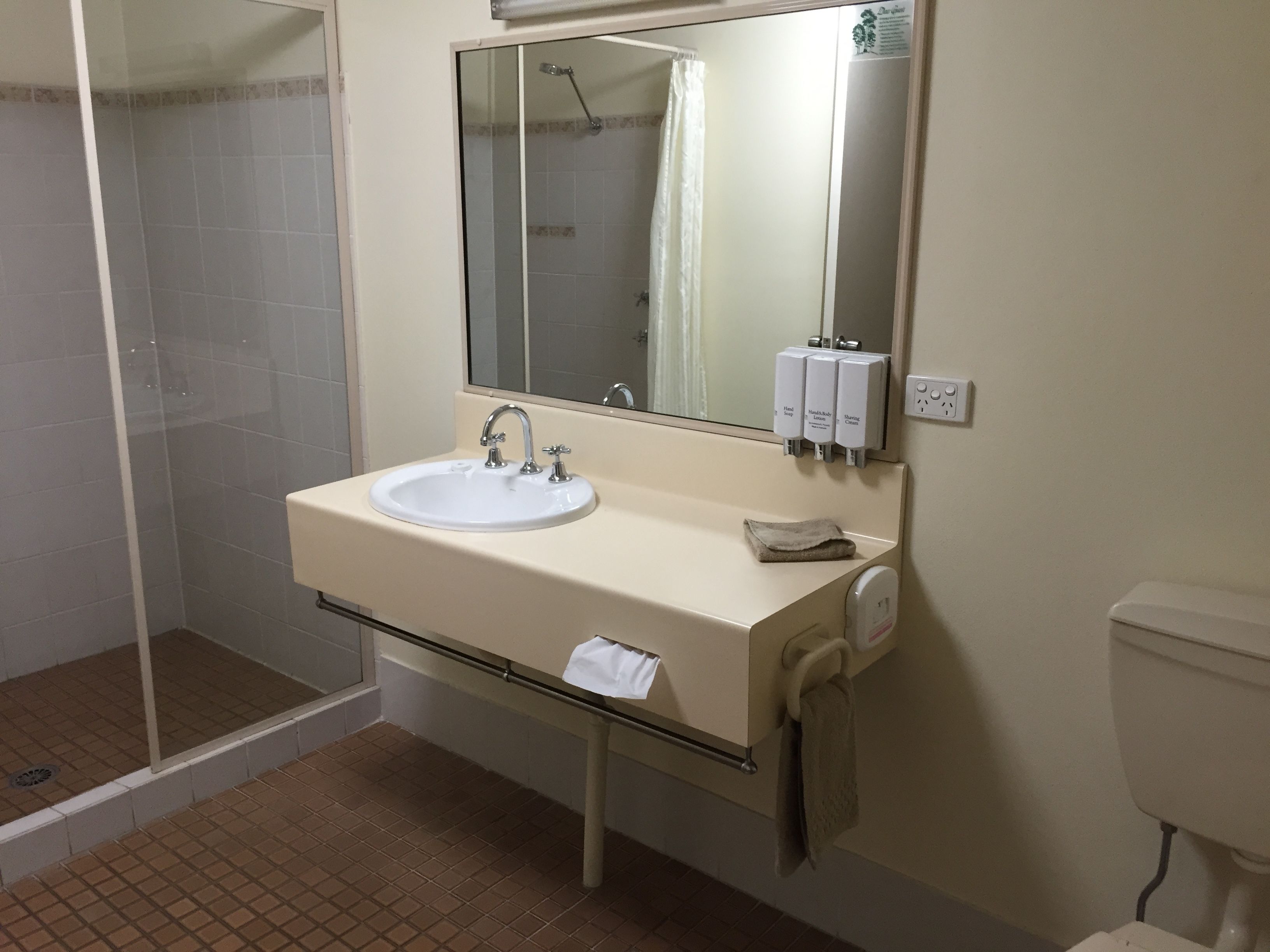 A bathroom with a sink, mirror, hand soap dispenser, and a towel hanging on a rack.