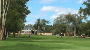 Un campo de golf con una casa al fondo, rodeado de árboles.