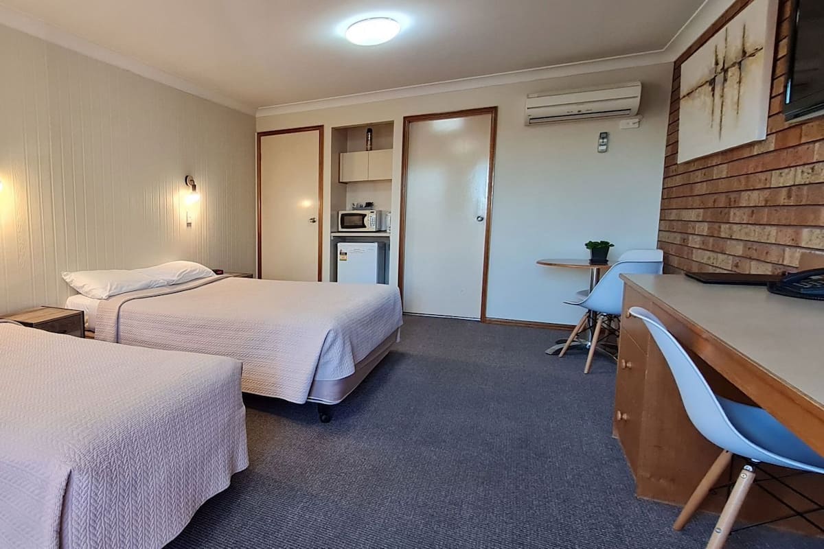 A hotel room with two beds, a desk, a chair, a microwave, and an air conditioning unit.