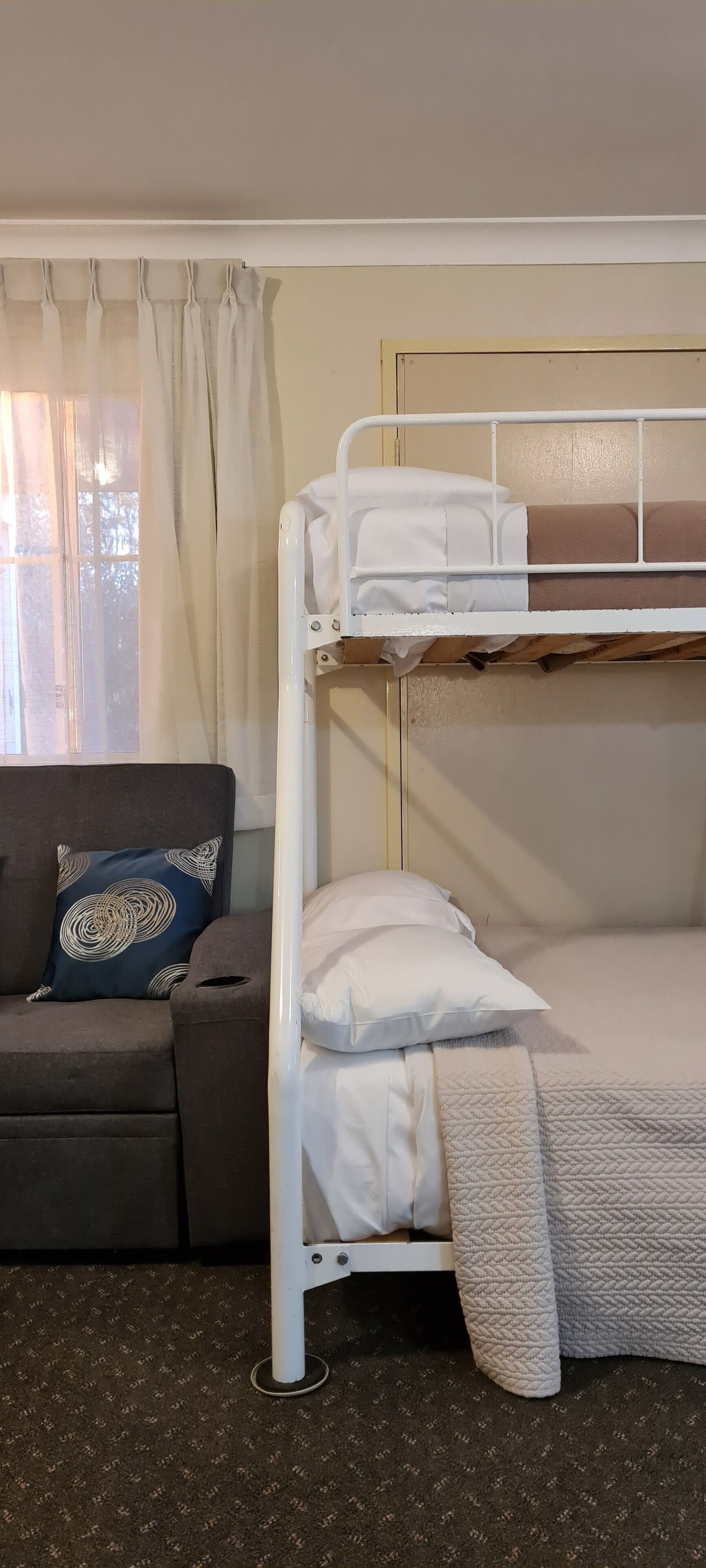 A bunk bed with a white frame, a sofa with a patterned cushion, and a window with curtains.