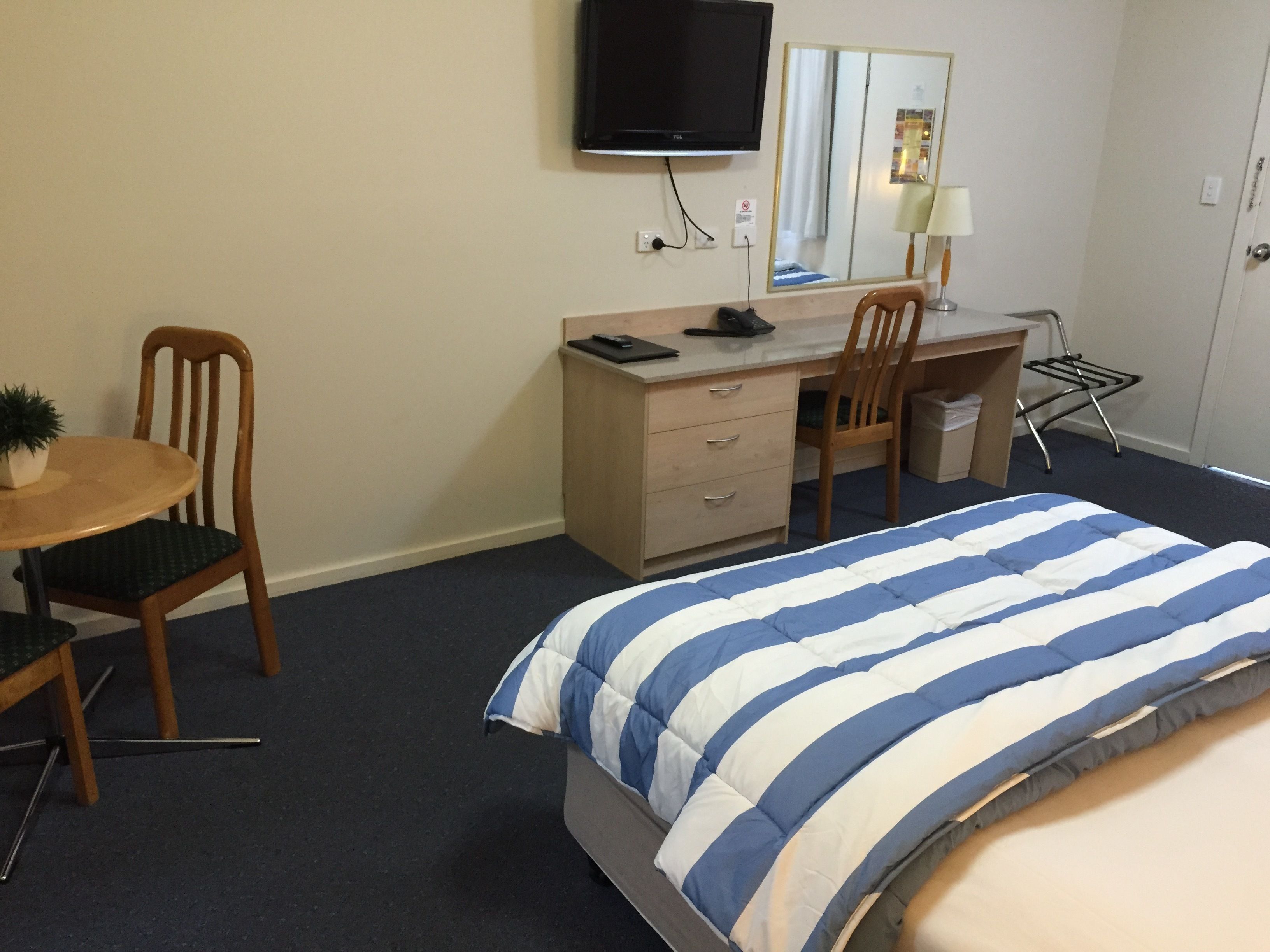 A hotel room with a bed, a desk, a chair, a TV, and a small table.