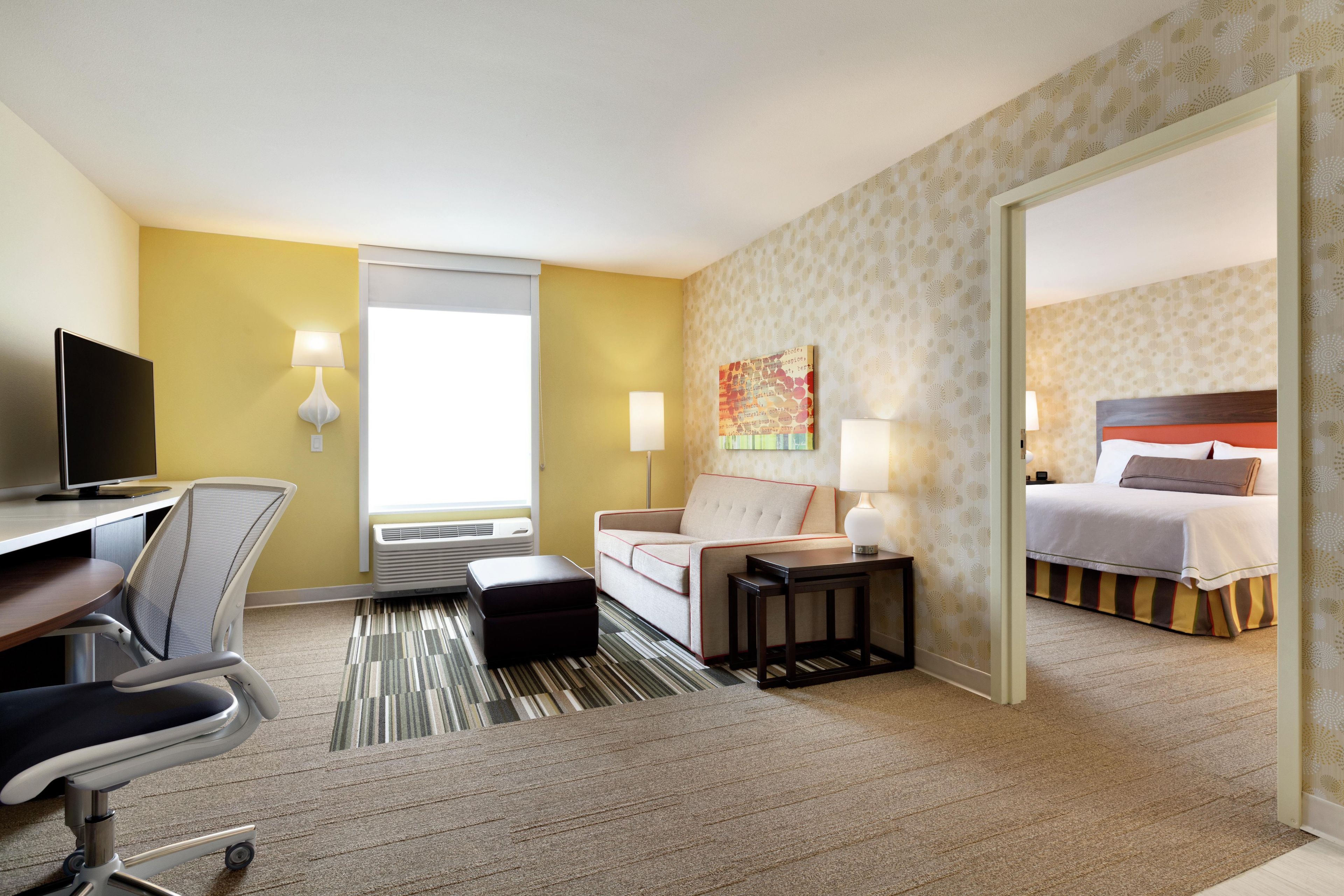 A hotel room with a bed, a desk with a chair, a sofa, a small table, a TV, and a window.