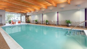 An indoor swimming pool with wooden beams, chairs, and potted plants. - Home2 Suites by Hilton Seattle Airport (Tukwila)