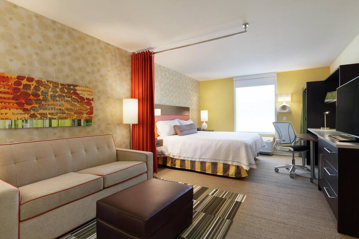 Une chambre d’hôtel avec un lit, un canapé, un bureau, une télévision et une fenêtre.