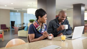 Two people sitting at a table in a modern indoor space with a laptop, a glass of orange juice, and a cup of coffee. - Home2 Suites by Hilton Seattle Airport (Tukwila)