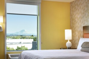 A hotel room with a bed, a nightstand with a lamp, a window with a view of a mountain, and a patterned wall.