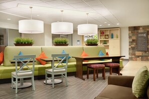 A modern lobby with a green sofa, two chairs, a wooden table, and potted plants.