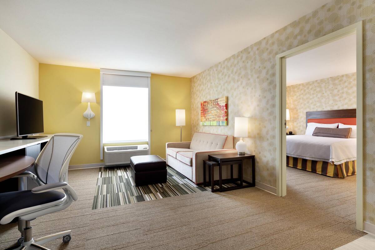 Une chambre d’hôtel comprenant un lit, un bureau avec une chaise, un canapé, une petite table, un téléviseur et une fenêtre.