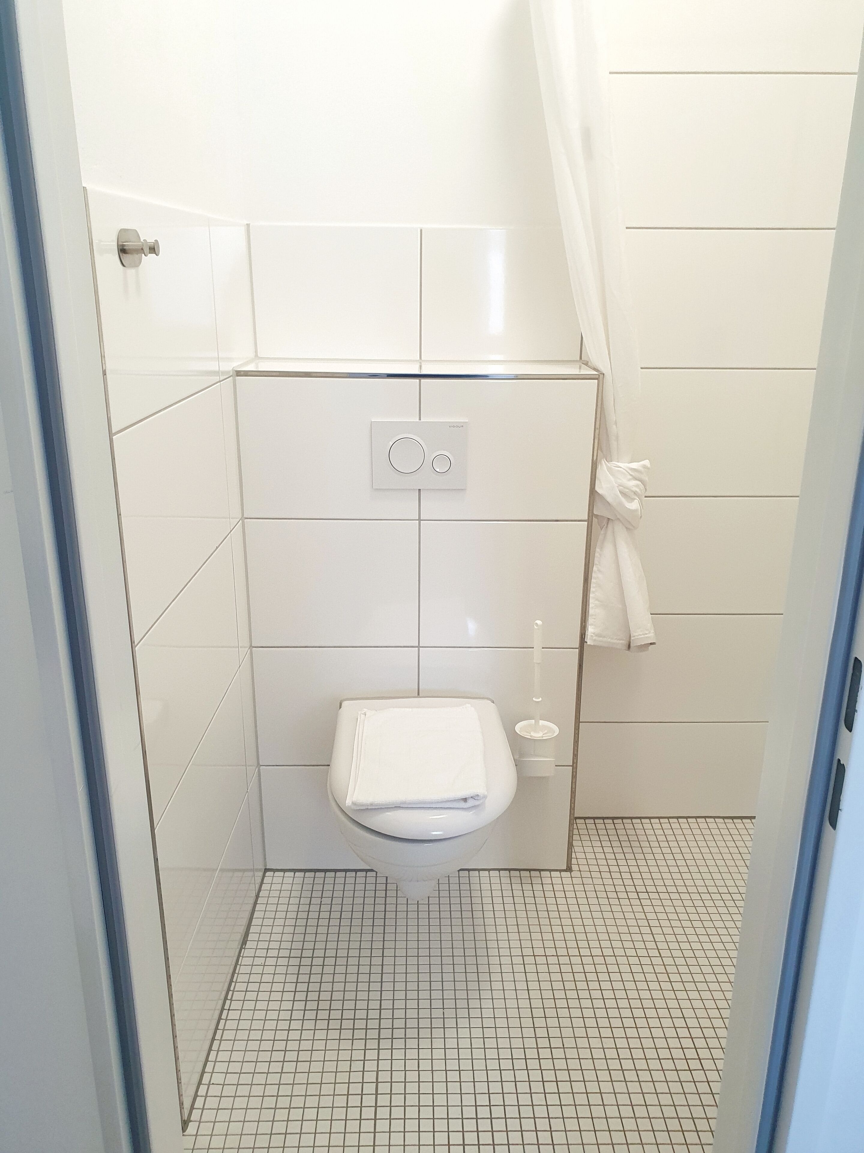 Ein kleines, weißes Badezimmer mit Toilette, Handtuchhalter und Bedienfeld.