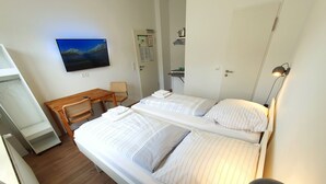 A hotel room with two beds, a desk, a chair, a TV, and a lamp. - Aparthotel Sanni  (Bremen)