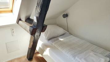 Una cama individual con ropa de cama a rayas, estructura de vigas de madera, un enchufe de pared y una ventana.