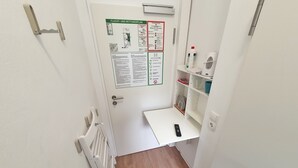 A narrow hallway with a white door, a small white shelf with a remote control, and a wall-mounted air conditioning unit. - Aparthotel Sanni  (Bremen)