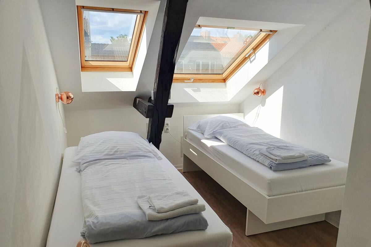 A small, modern room with two beds, skylights, and a wooden floor.