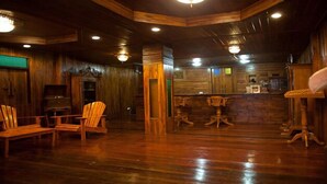Un interior de madera con una zona de bar, sillas de madera y una mesa central.