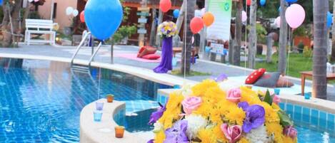 Un área de piscina con un edificio de madera al fondo, rodeada de palmeras y decorada con globos.